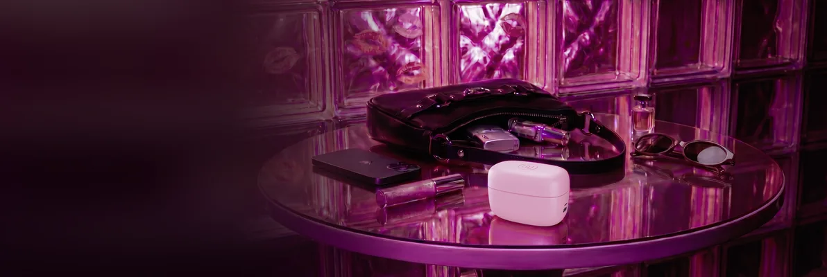 Un sextoy discret dans un étui rose, posé sur une table en verre à côté d'un sac à main, d'un rouge à lèvres et de lunettes de soleil